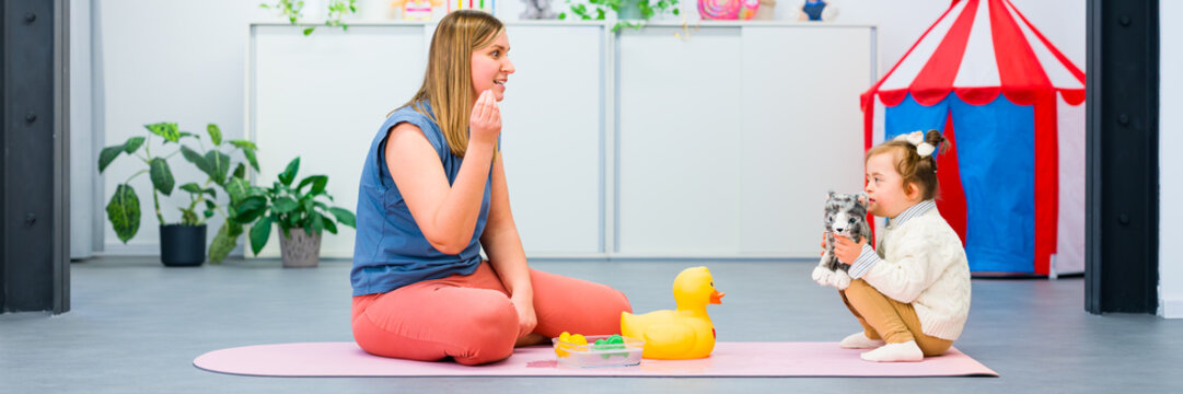 Nonverbal child with Down syndrome learning baby sign language with the help of a speech therapist. Child therapy, neurodiversity, learning difficulty, developmental disability.
