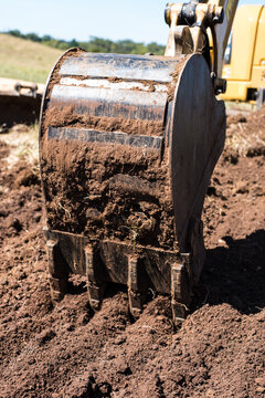 Toothed excavator bucket digging in brown soil