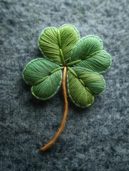 Hand embroidered green four-leaf clover on grey fabric background