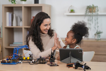 african kid learning robot circuits on tablet computer,caucasian tutor helps a student in STEM lesson in class,teacher and child giving high five together