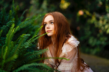 Beautiful red head girl in pink  vintage dress  standing near green plants and fern. Art work of...
