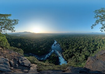 Breathtaking Aerial View of Dense Tropical Forest with Flowing River Beneath a Clear Sky and Distant Mountains at Sunrise