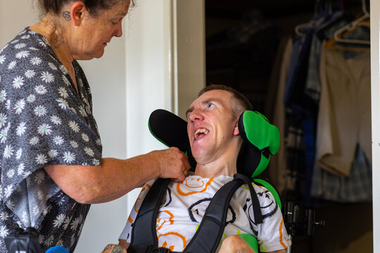 Middle aged woman fixing wheelchair strap on son with disability