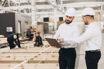 Engineers using laptop while inspecting modular building construction in factory
