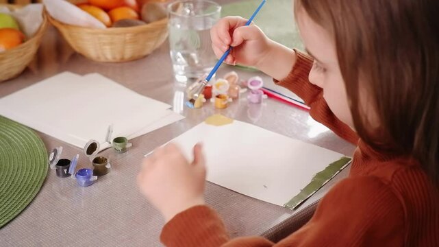 Young girl painting on a white sheet of paper with tempera colors