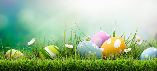 Six painted easter eggs celebrating a Happy Easter on a spring day with a green grass meadow, bright sunlight and a cool colour background with copy space.