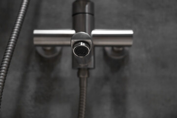 Close-up of a stainless steel shower faucet featuring a flexible metal hose, mounted on a textured...