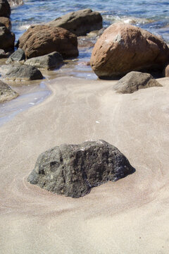 The selected region shows a dark, weathered rock resting on a sandy beach, consistent with a water-worn extrusive igneous rock like basalt. La speranza Beach Villanova Alghero Sardinia
