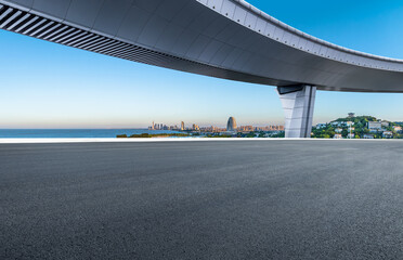 Empty asphalt road under an overpass with city skyline view
