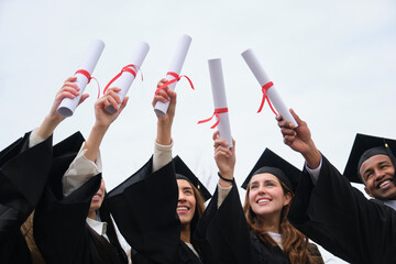 Group of cheerful multiethnic graduates celebrating graduation holding their diplomas up in the air