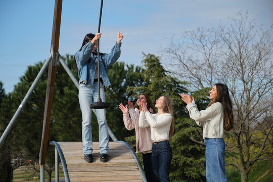 Group of friends having fun in a playground, one girl using a zip line and the others clapping
