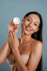 Cream for the skin in hand. Young woman is in the studio against background