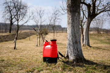 Bright red sprayer standing in a sunny spring garden. Gardening equipment concept