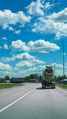 Cement truck is driving down a road with a blue sky in the background