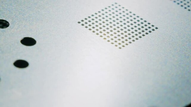 Macro 4K shot at 30fps of a technician holding a metal stencil with paste applied on a CPU microchip, demonstrating the process of heating and using the paste in microelectronics.