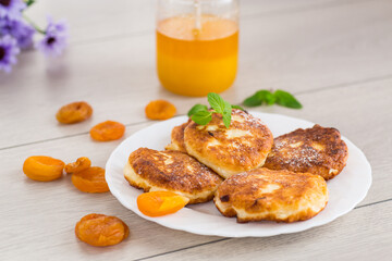 Cottage cheese pancakes with dried apricots and honey on a wooden table