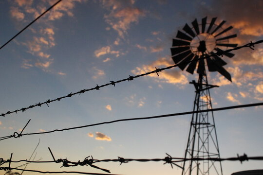 Silhouette wire fence at sunset with a windmill in the background