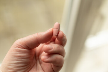 A hand holding a pill between the fingers