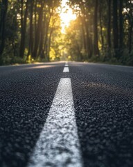 Fototapeta premium Serene journey through sunlit forest road with central white line marking asphalt path toward bright light