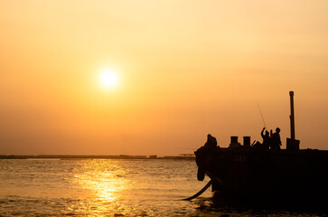 Two fishermen cast their lines on a wrecked boat at Muara Angke, Jakarta. Their silhouettes...