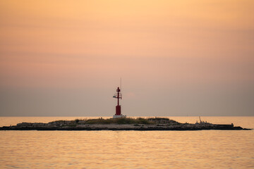 Secluded small island with lighthouse inrays of setting sun near Porec, Croatia.Calm sea, sky is...