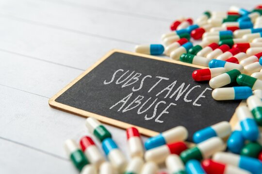 A chalkboard with the words "SUBSTANCE ABUSE" surrounded by scattered pills and capsules. Medical and healthcare concept.