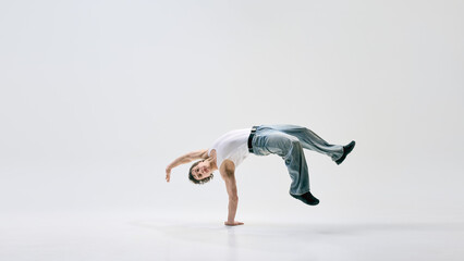 Street performer flipping effortlessly with sharp body control expressing passion through movement against white background. Concept of music, art, sport, urban style, creativity, modern artistry.