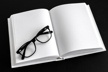 Black reading glasses are lying on a white notepad. Space for text