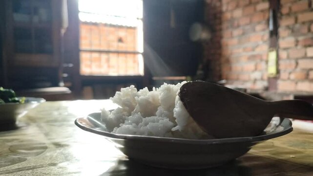 A plate of warm rice with a ladle on top and steam coming out in a country kitchen with a window in the background with sunlight coming in