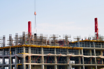 Construction site with workers assembling concrete monolith high-rise structure, scaffolding, industrial equipment, and architectural framework in progress.