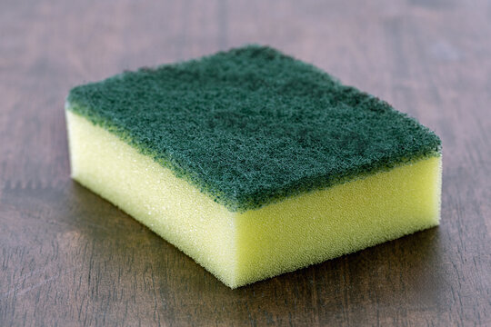 Green rectangular scouring pad with yellow sponge is used for cleaning cups and bowls.