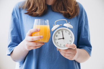 Girl in a blue T-shirt with glass of orange juice and alarm clock, close up.