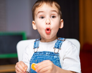 Child expresses joy while eating candy. A young boy with short hair in overalls looks delighted...