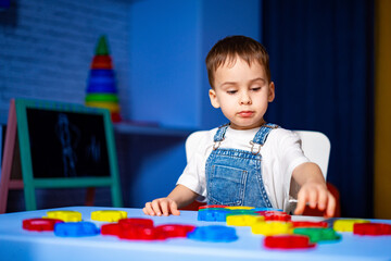 Child playing with bright blocks. A young boy in denim overalls focused on arranging colorful...
