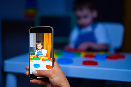 Kid with colorful shapes. A child is engaged in creative play, manipulating colorful shapes while an adult captures the moment on a phone.