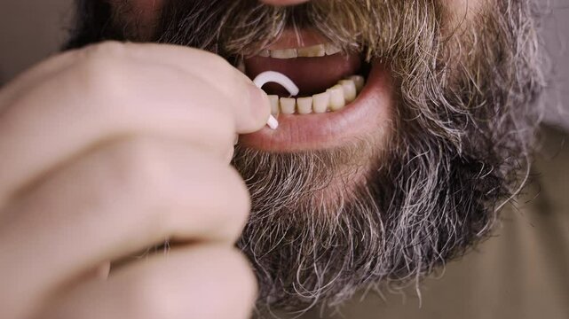bearded caucasian man cleaning teeth using dental floss pick