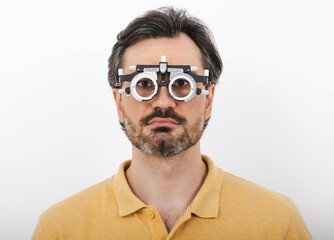Obraz premium Middle-aged man wearing optometrist trial frame to select glasses for vision treatment, isolated on white. Ophthalmology
