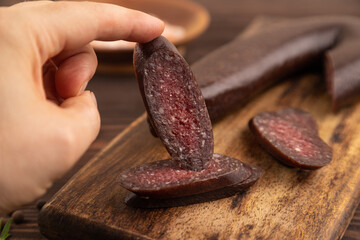 Sujuk sausage with hand on wooden cutting board with pepper and herbs on brown wooden. Side view,...