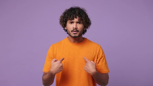 young Indian man wear orange t-shirt casual clothes look camera pointing fingers herself ask say who me no thanks i do not need it isolated on plain pastel light purple background. Lifestyle concept