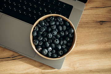 A laptop on the table and a bowl of fresh blueberries as a snack.