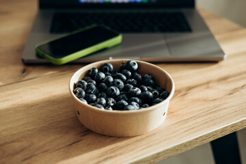 A laptop on the table and a bowl of fresh blueberries as a snack.