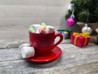 a red cup filled with marshmallow slices. There is a Christmas tree in the background
