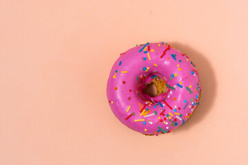 Pink donut with colorful sprinkles on pastel beige background.