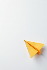 A solitary, handcrafted paper airplane, crafted from bright yellow paper, rests on a pristine white surface, poised for flight, symbolizing dreams of journey and exploration.