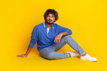 Portrait of a young handsome man in casual clothing seated against a vibrant yellow background,...