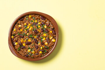Traditional Mexican Chili con carne. Minced meat and vegetables stew in tomato sauce on yellow background. Top view. Copy space