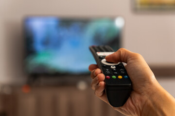 A hand holds and presses the TV remote control, changing the channel
