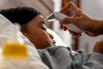 A mother checking her sick child's temperature using a digital thermometer