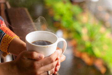 A woman is relaxing while drinking hot coffee on his balcony terrace in the tropical morning...