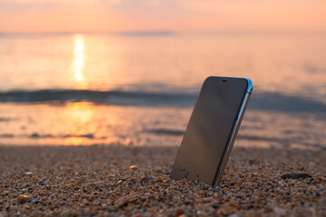 Lost smartphone device at sandy beach in summer sunrise